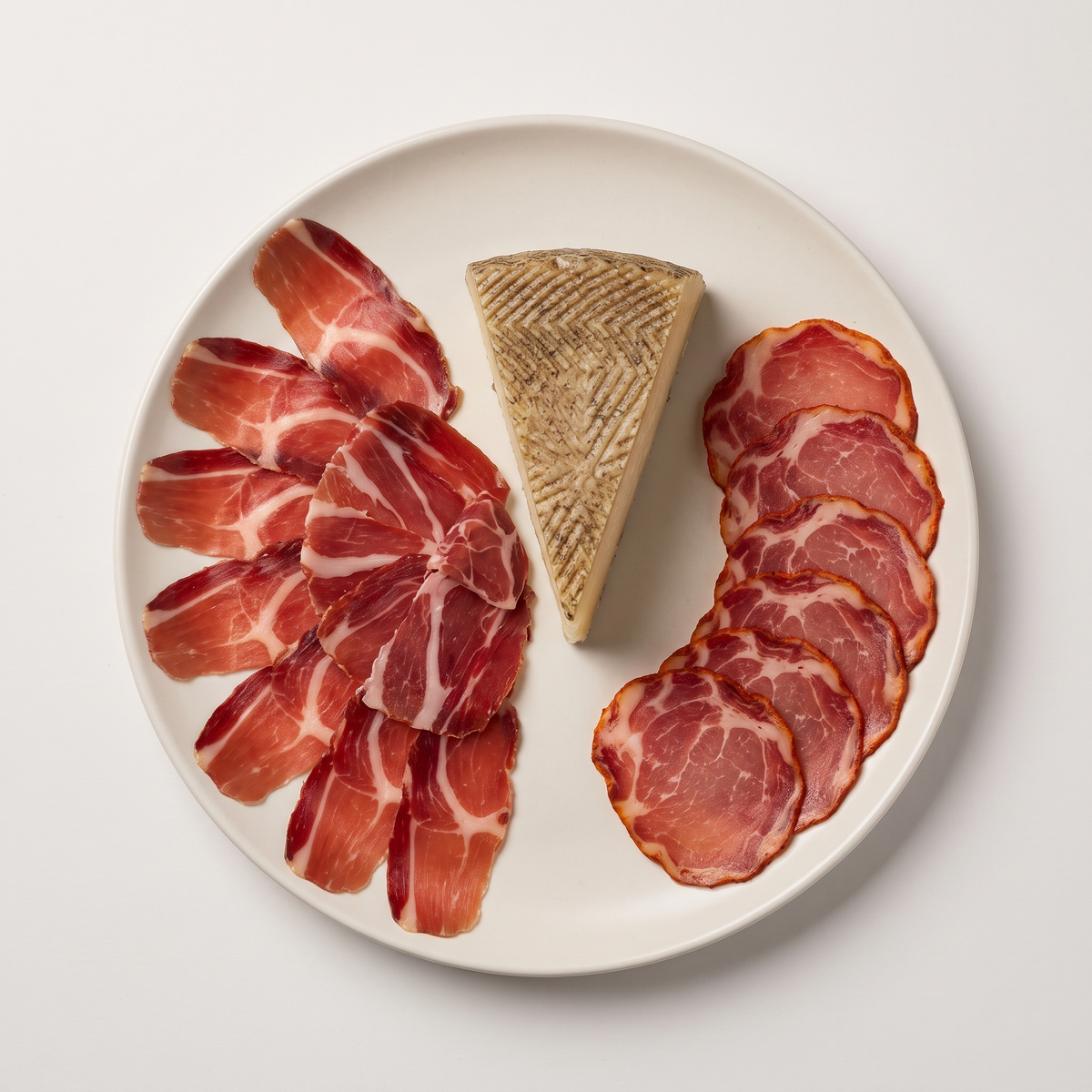 Bellota Charcuterie Selection — Jamón Ibérico, Lomo, and Manchego cheese plated with rosemary sprig and wooden spoon on linen